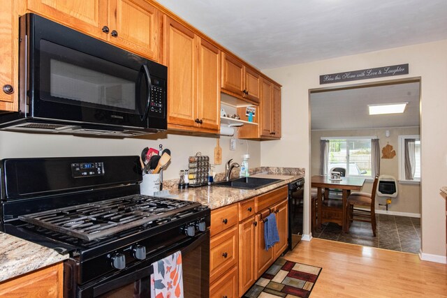 kitchen with black appliances, a sink, light stone counters, and baseboards