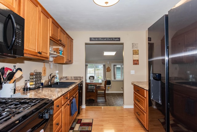 kitchen with black appliances, a sink, brown cabinets, light wood-style floors, and light stone counters
