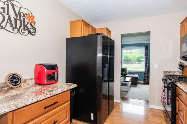 kitchen featuring black appliances, light wood finished floors, baseboards, light stone counters, and brown cabinetry