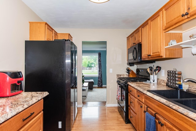 kitchen featuring black appliances, light wood-style flooring, a sink, open shelves, and brown cabinetry