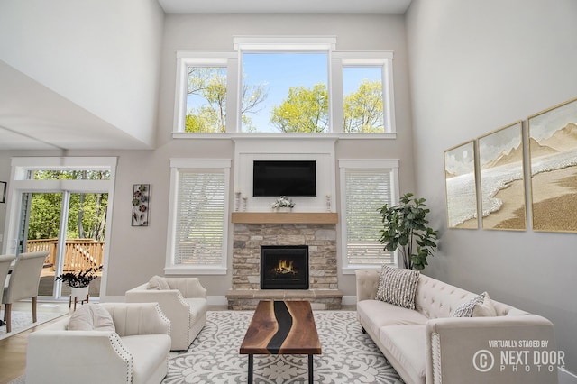 living area featuring a fireplace, healthy amount of natural light, a towering ceiling, and wood finished floors