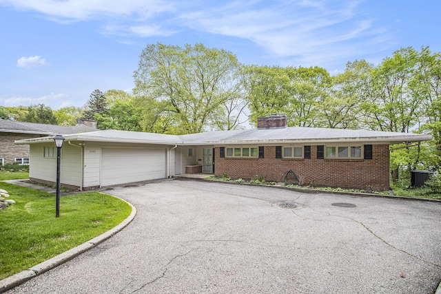 ranch-style home with a chimney, driveway, a garage, and brick siding