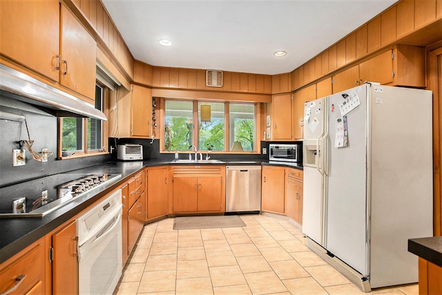 kitchen featuring white appliances, dark countertops, a sink, light tile patterned flooring, and recessed lighting