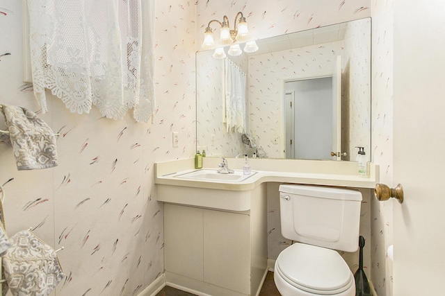 half bathroom featuring toilet, wallpapered walls, vanity, and baseboards
