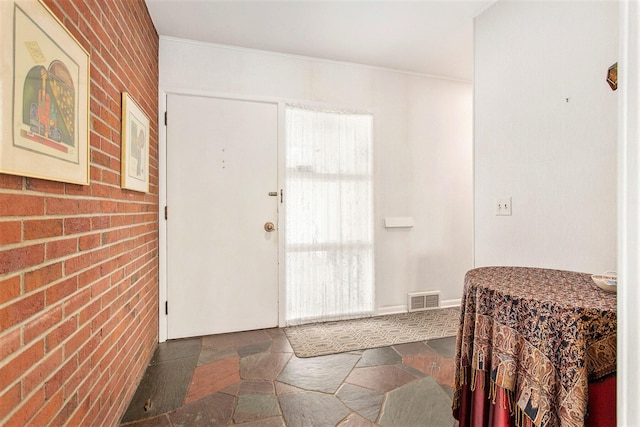 foyer entrance featuring stone tile floors, brick wall, and ornamental molding