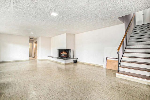 unfurnished living room with baseboards, a multi sided fireplace, and stairs