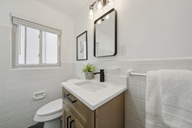 bathroom featuring tile walls, toilet, wainscoting, and vanity