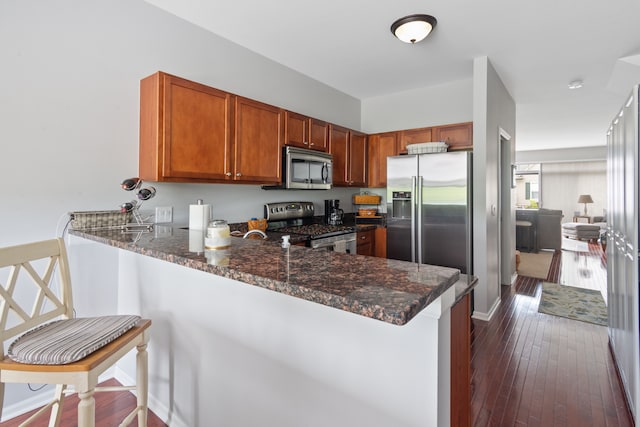 244 Wright St Unit 77, Wixom, MI 48393 - kitchen featuring appliances with stainless steel finishes, a peninsula, dark stone counters, brown cabinetry, and dark wood-style flooring