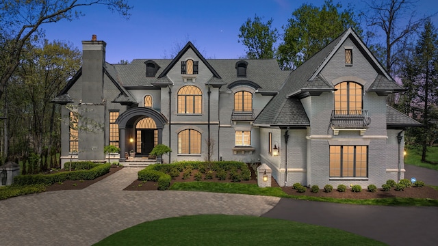 french country home featuring a chimney, brick siding, and a balcony