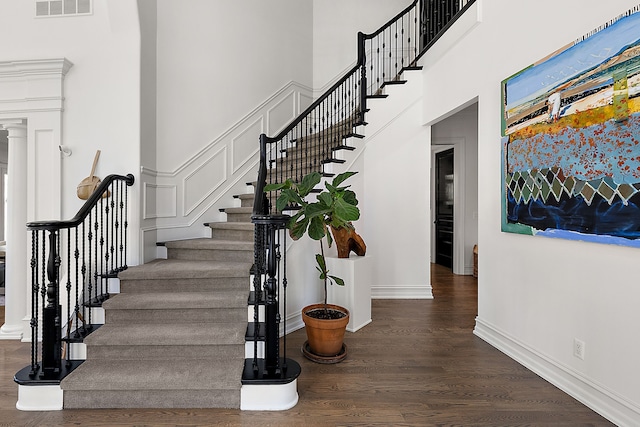 stairway with a towering ceiling, wood finished floors, ornate columns, and baseboards