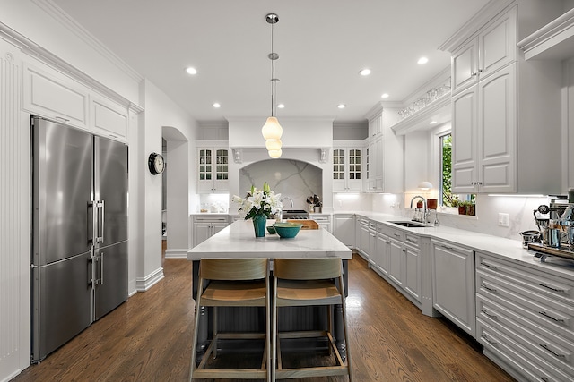 kitchen featuring high end refrigerator, a sink, white cabinetry, tasteful backsplash, and glass insert cabinets