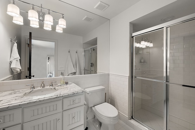 bathroom featuring a shower stall, toilet, vanity, tile walls, and a wainscoted wall