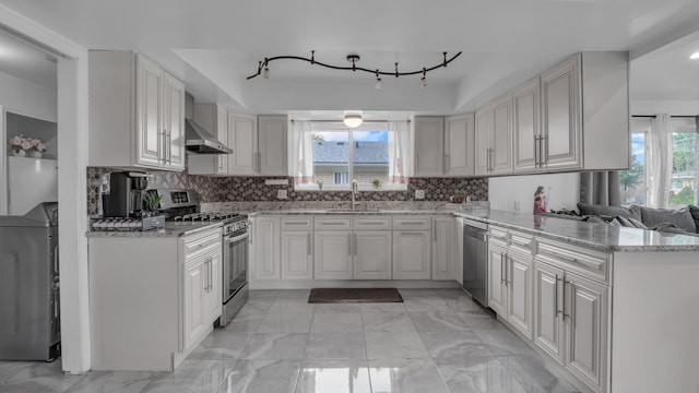 kitchen featuring appliances with stainless steel finishes, healthy amount of natural light, a sink, and light marble finish flooring