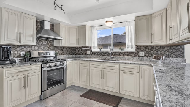 kitchen featuring gas stove, a sink, wall chimney range hood, cream cabinetry, and backsplash