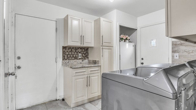 washroom featuring water heater, separate washer and dryer, cabinet space, and light marble finish flooring