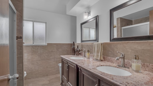 bathroom with toilet, an enclosed shower, tile walls, double vanity, and a wainscoted wall