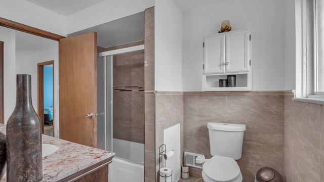 full bathroom featuring toilet, enclosed tub / shower combo, vanity, tile walls, and a wainscoted wall