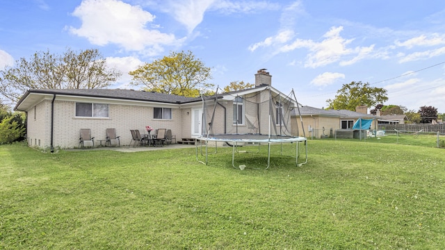rear view of house with a trampoline, a patio, brick siding, and a chimney