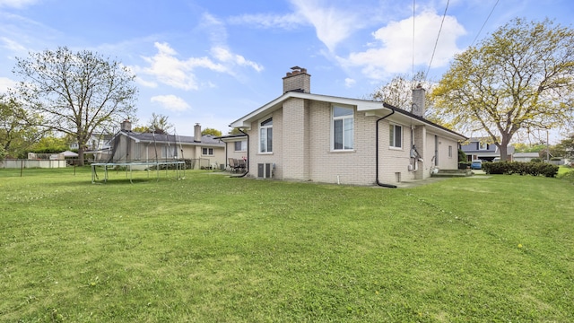 rear view of property featuring a trampoline, a chimney, brick siding, and a yard