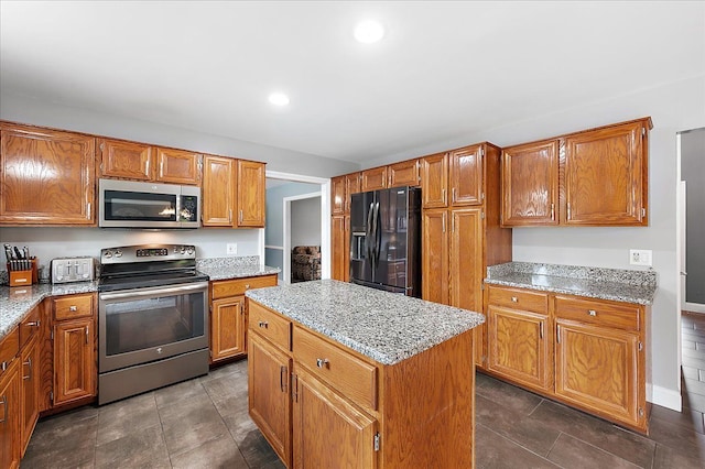 kitchen featuring appliances with stainless steel finishes, a center island, brown cabinetry, light stone counters, and recessed lighting
