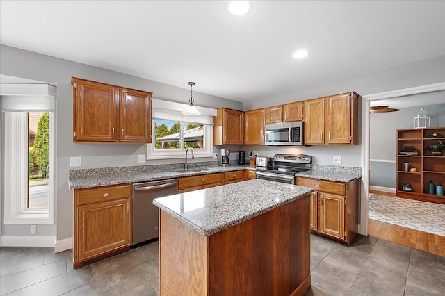 kitchen featuring stainless steel appliances, a sink, baseboards, light stone countertops, and hanging light fixtures