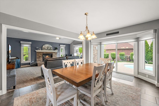 tiled dining room featuring a chandelier, a fireplace, baseboards, a ceiling fan, and vaulted ceiling