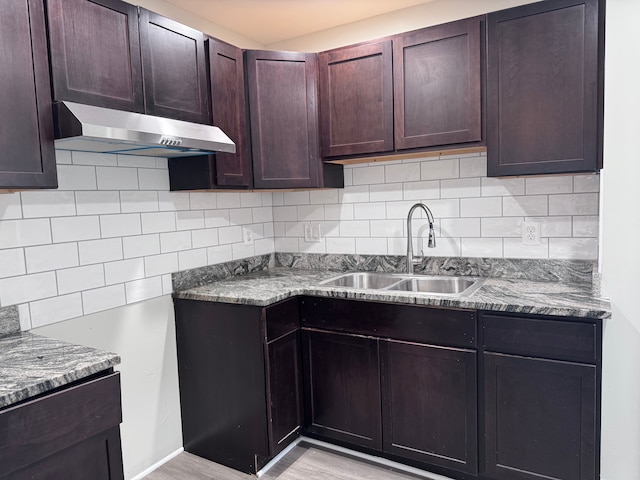 kitchen featuring under cabinet range hood, a sink, backsplash, dark brown cabinetry, and light wood-style floors