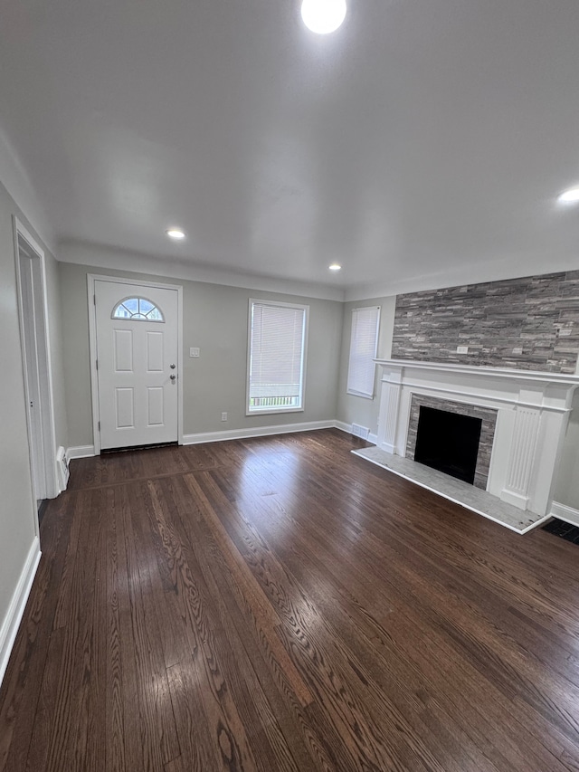 unfurnished living room with a fireplace with raised hearth, dark wood-style floors, baseboards, and recessed lighting