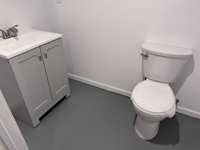 half bathroom with vanity, toilet, finished concrete flooring, and baseboards