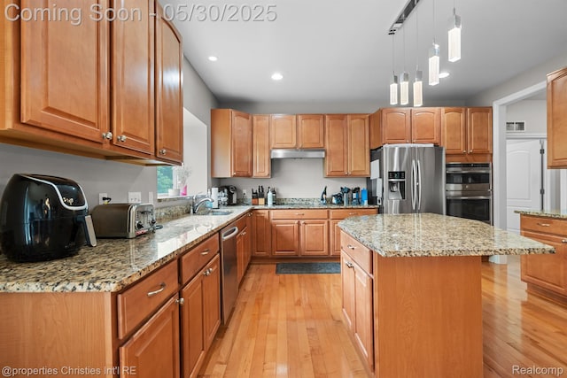 24516 Cavendish Ave E, Novi, MI 48375 - kitchen featuring appliances with stainless steel finishes, light stone countertops, light wood-style flooring, under cabinet range hood, and a center island