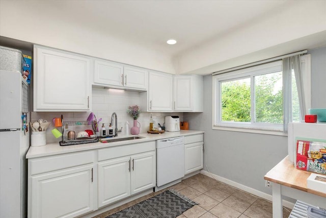 kitchen featuring white appliances, a sink, backsplash, white cabinetry, and light countertops