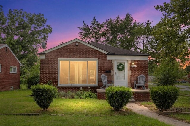 view of front of home with brick siding and a yard
