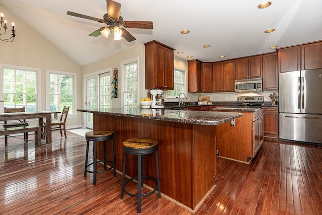 kitchen with appliances with stainless steel finishes, a kitchen island, dark wood-type flooring, a sink, and vaulted ceiling