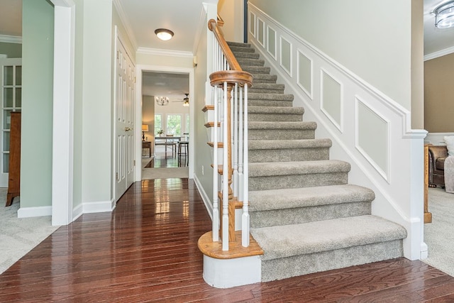 stairway with ornamental molding, wood finished floors, carpet flooring, and ceiling fan