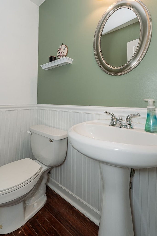 half bathroom featuring hardwood / wood-style flooring, toilet, a sink, and baseboards