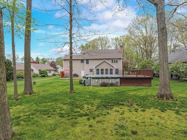 rear view of house featuring a chimney, a wooden deck, a yard, and roof with shingles