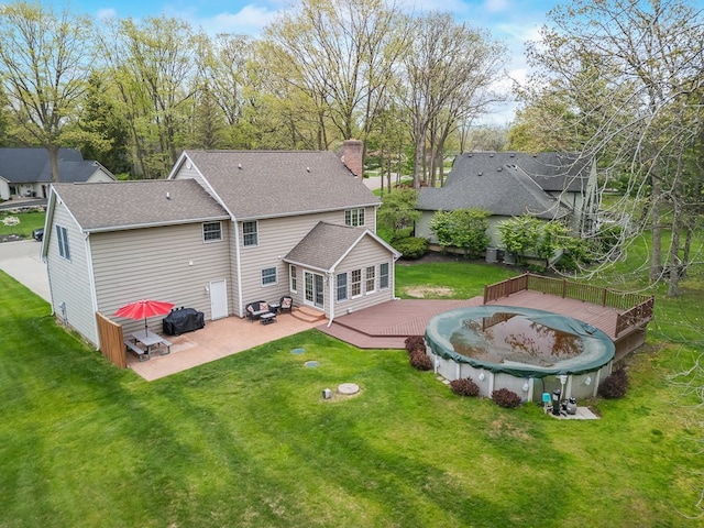 rear view of house featuring a deck, a patio area, a chimney, and a yard