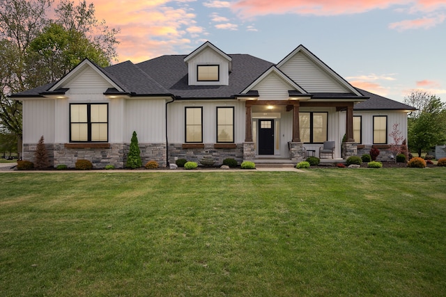 view of front facade with stone siding, a porch, a yard, and roof with shingles