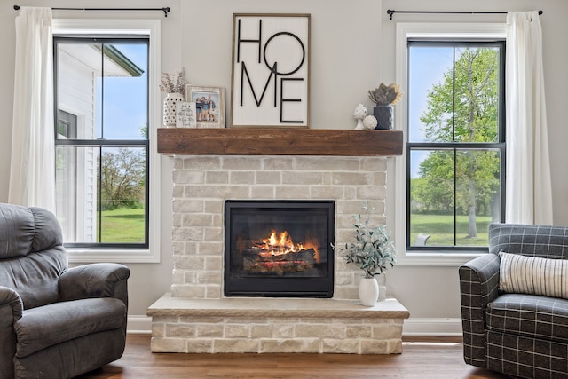 living area with baseboards, wood finished floors, a fireplace, and plenty of natural light