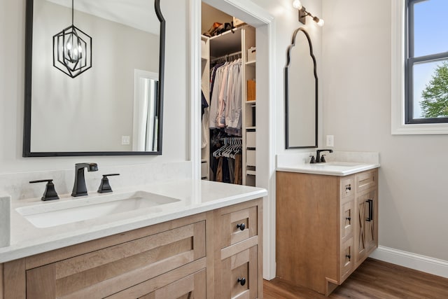full bath featuring two vanities, a spacious closet, wood finished floors, and baseboards