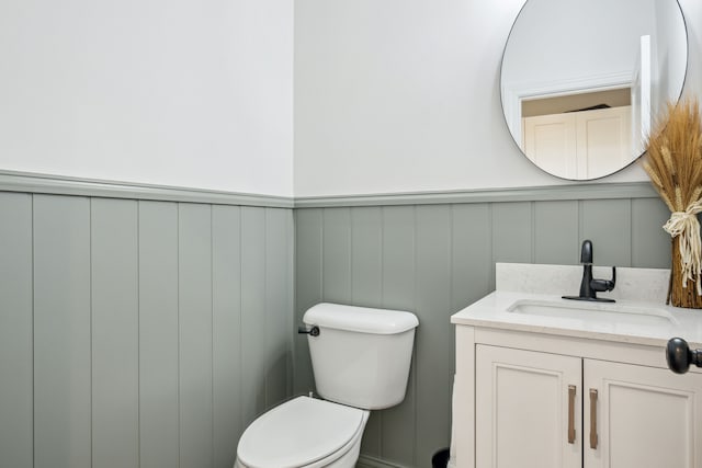 bathroom featuring a decorative wall, vanity, toilet, and a wainscoted wall