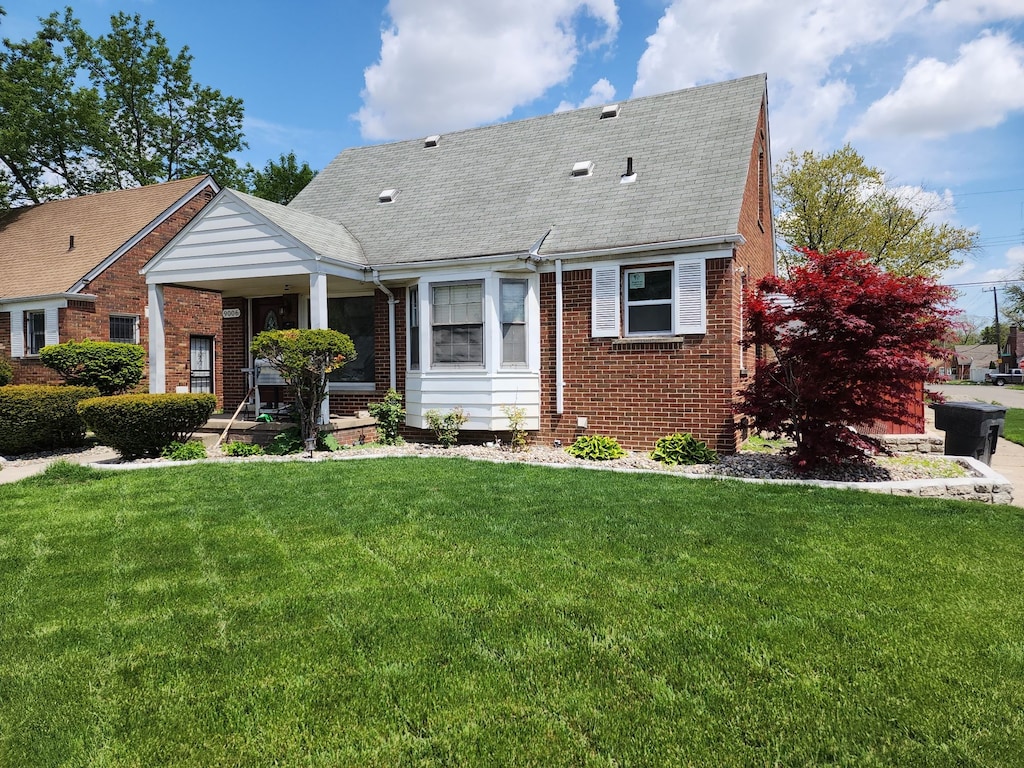 9006 Grandville Ave, Detroit, MI 48228 - view of front of house featuring brick siding, a front yard, a shingled roof, and a porch