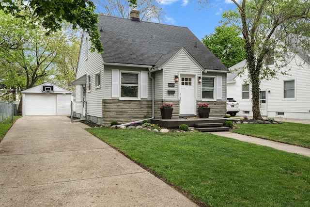 view of front of house with a shingled roof, an outbuilding, a detached garage, stone siding, and a front lawn