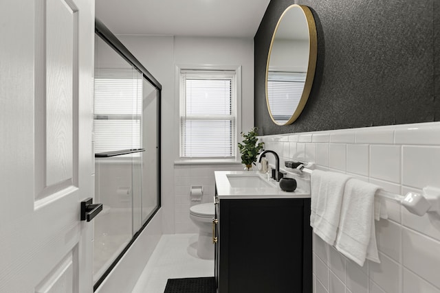 full bathroom with tile walls, toilet, vanity, shower / bath combination with glass door, and wainscoting