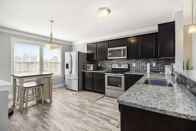 kitchen with stainless steel appliances, a sink, light stone countertops, decorative backsplash, and baseboards