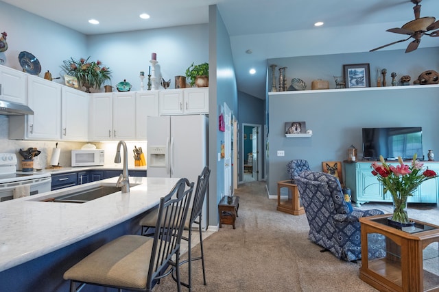 kitchen with white appliances, light colored carpet, a sink, under cabinet range hood, and white cabinets