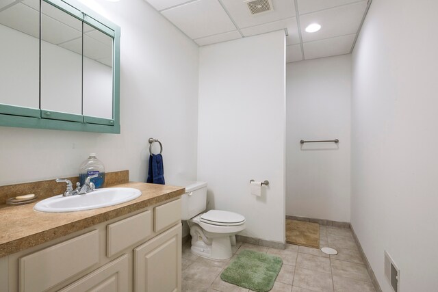 bathroom with toilet, vanity, tile patterned flooring, a paneled ceiling, and baseboards