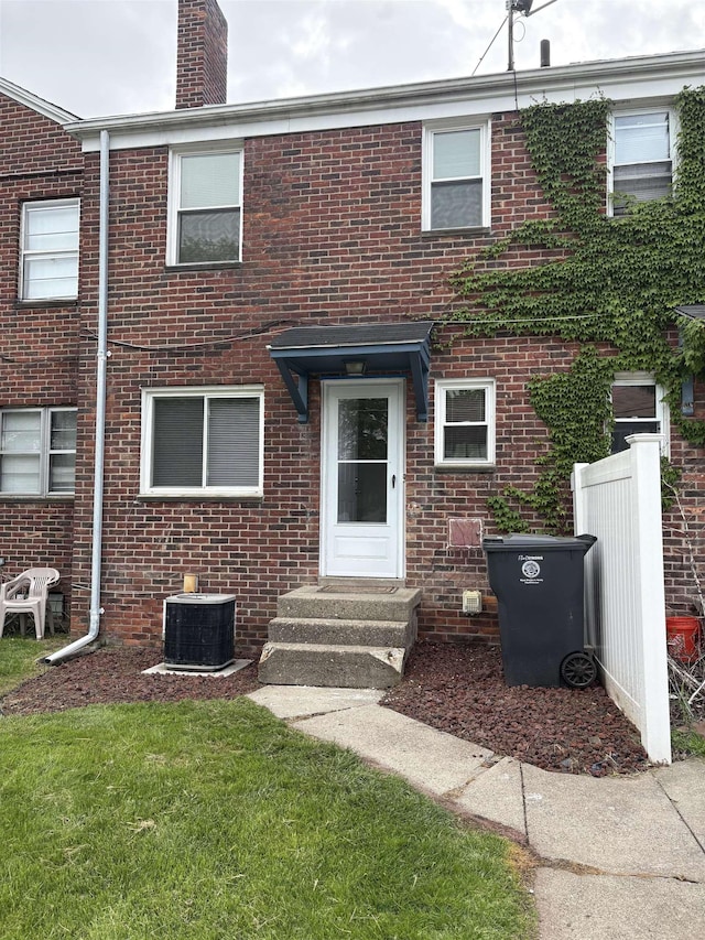 view of front of house with central AC unit, brick siding, and a chimney
