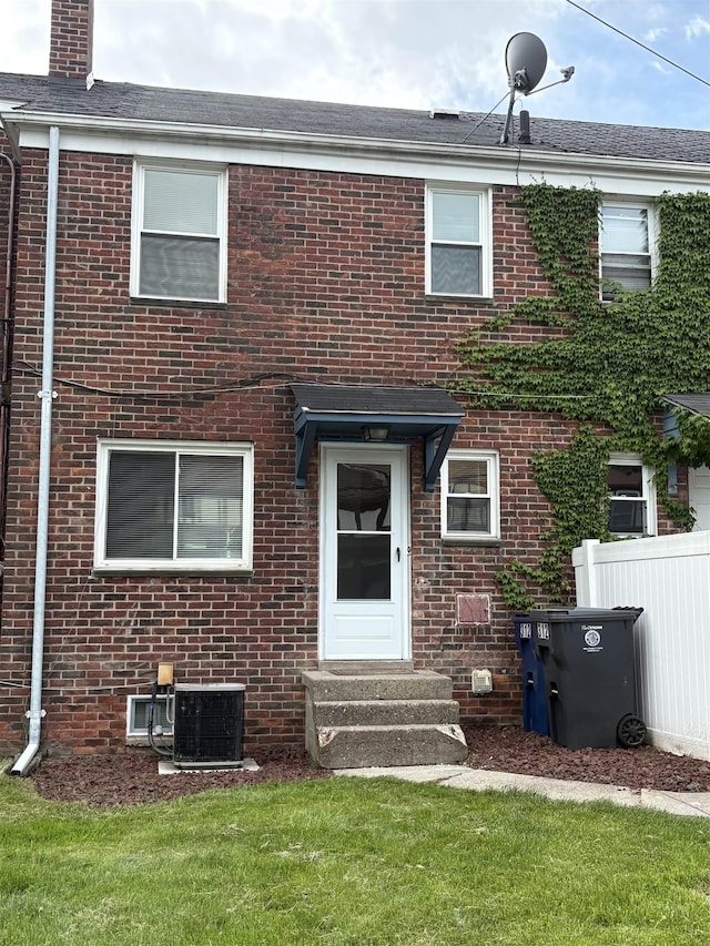 back of house featuring cooling unit, brick siding, fence, and a chimney