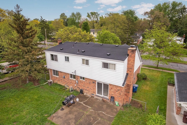 back of house with a patio, brick siding, a yard, a chimney, and view of wooded area